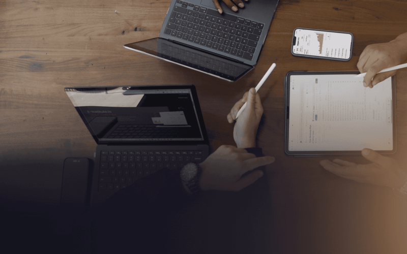 Overhead view of industry experts collaborating with digital devices—tablet, smartphone, and laptop—showcasing E-Institute's cutting-edge e-learning platform focused on e-commerce, wholesale, and investment education.